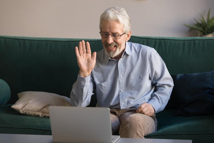 Senior man on a video call waving at a laptop
