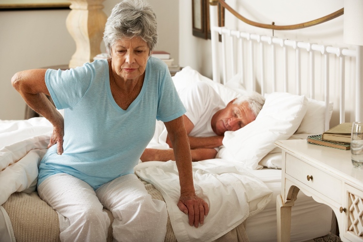 Senior woman sitting on the edge of the bed holding lower back