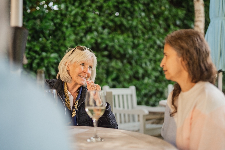Two senior women in a garden drinking wine